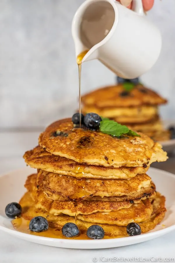 pouring maple syrup on Fluffy Keto Blueberry Pancakes Recipe