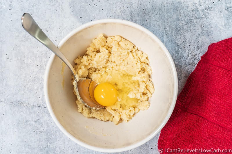 adding egg to dough for Keto Magic Cookie Bars Recipe