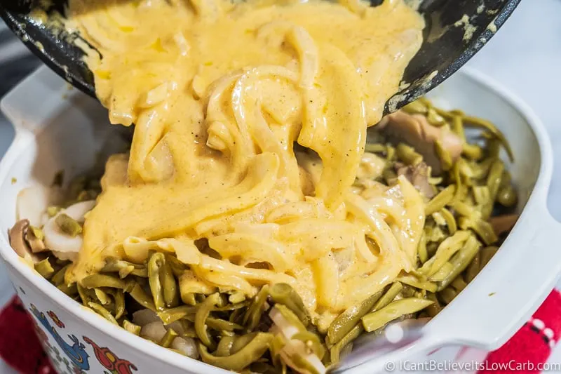 pouring cheese sauce over low carb Green Bean Casserole
