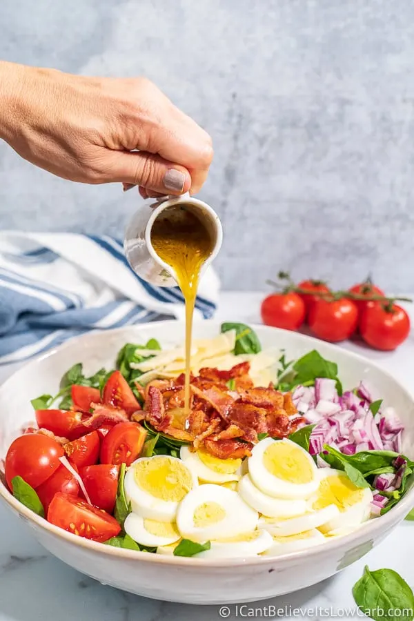 pouring dressing over a Spinach Salad with egg