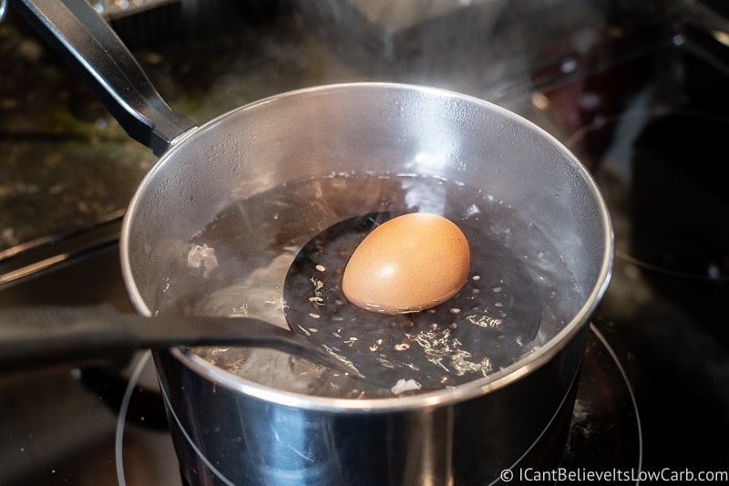 lowering an egg into boiling water to be boiled