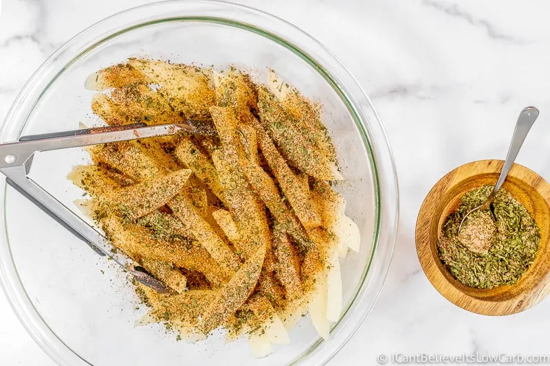 covering Keto Jicama Fries with spices