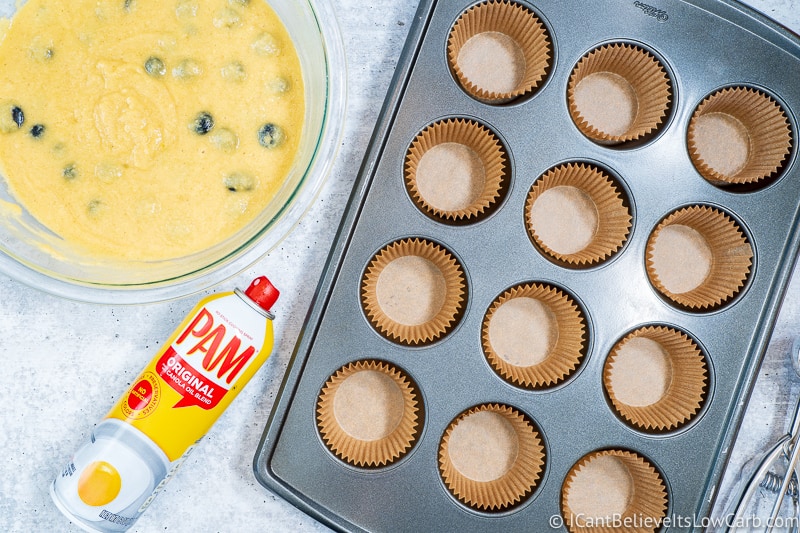 muffin pan with a bowl of Keto Blueberry Muffin batter and pam spray