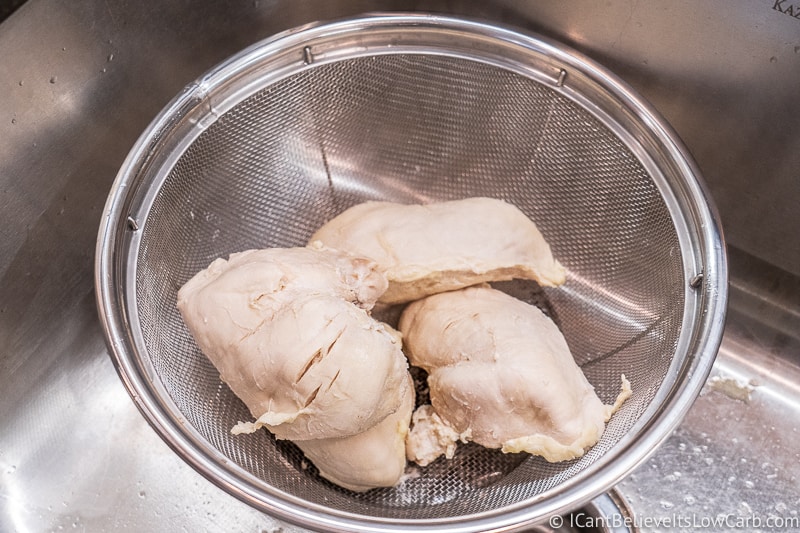 poached chicken in colander in the sink