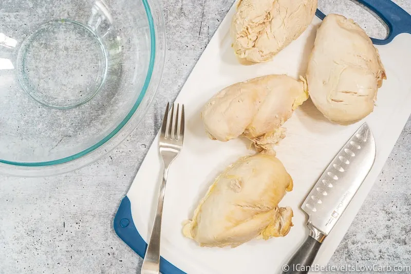 poached chicken on a cutting board with fork and knife