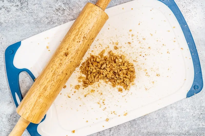 crushing walnuts on a cutting board with rolling pin