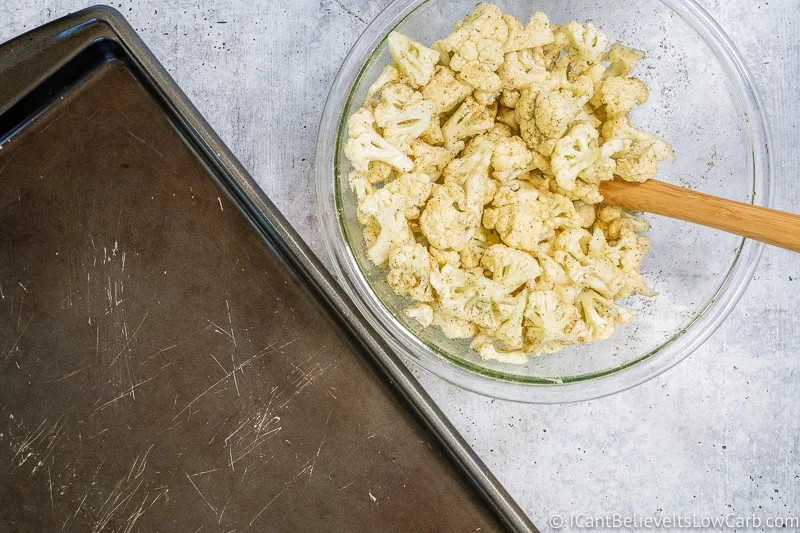 Bowl of raw seasoned Cauliflower and empty sheet pan