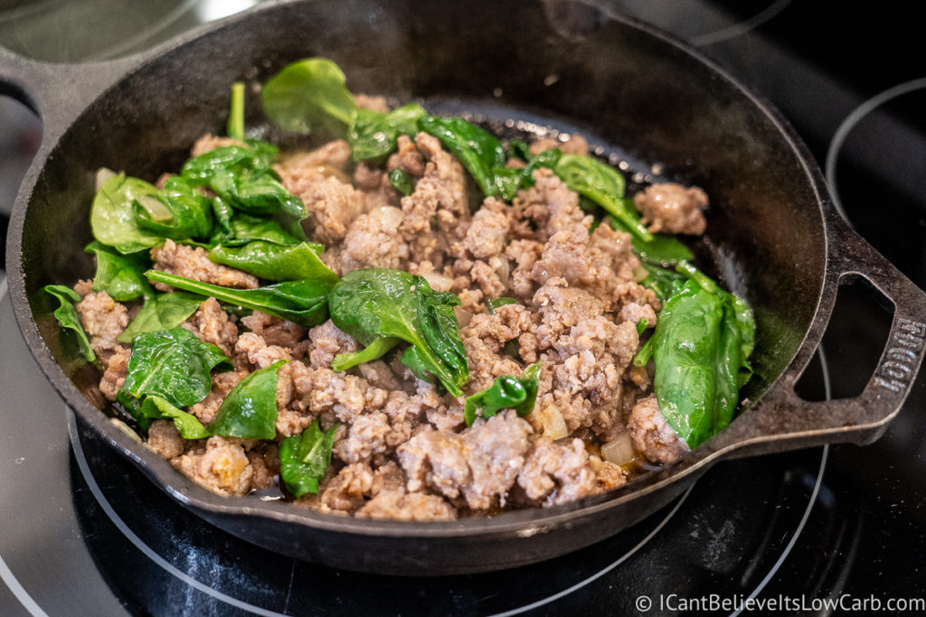 Frying sausage and spinach in a pan