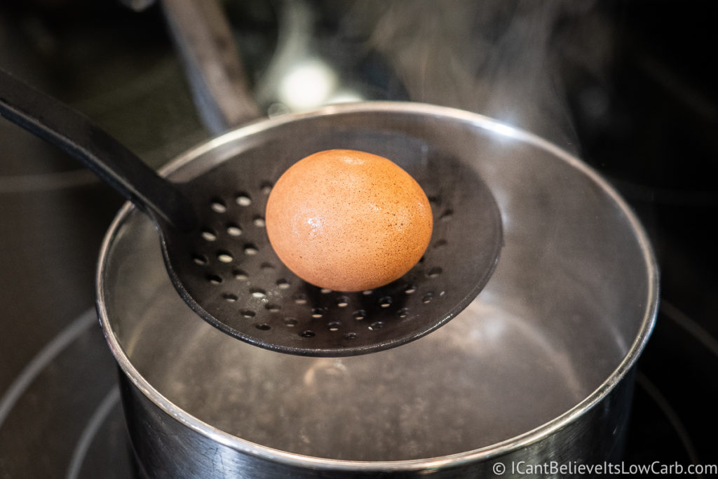 lowering an egg into a pot of boiling water