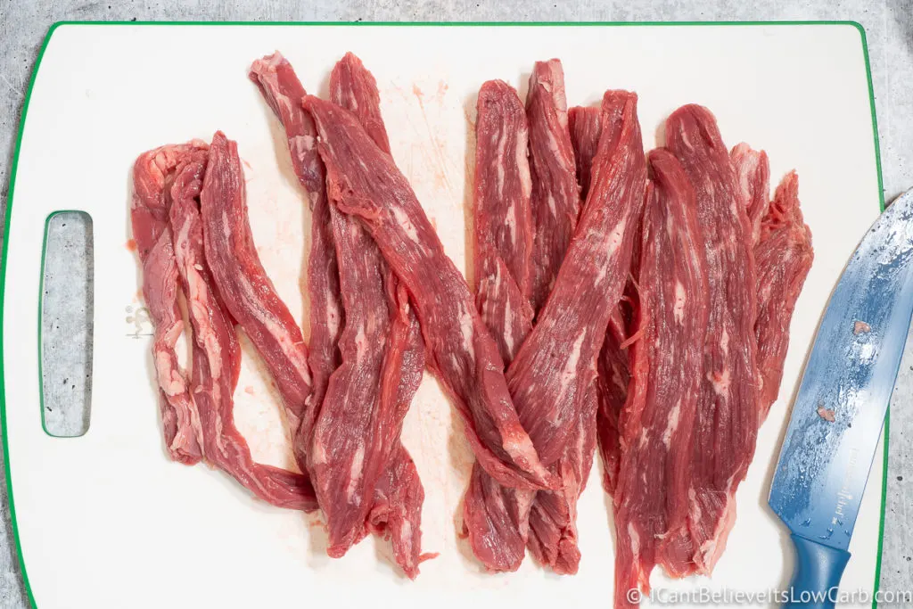 cutting beef into strips on a cutting board