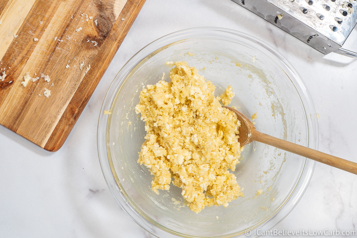 Mixing frozen butter with keto biscuit ingredients in a bowl